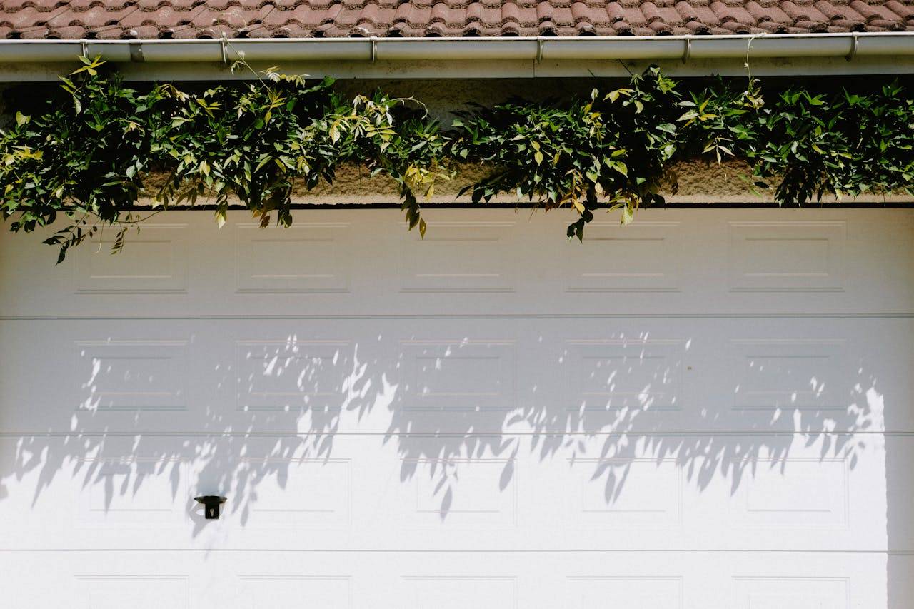 hero-img-01 A closed white garage door adorned with lush green foliage casting shadows.