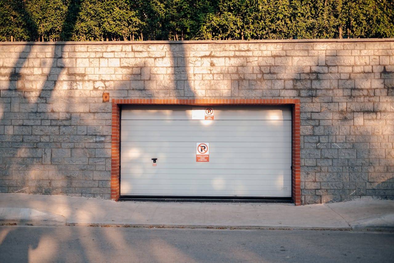 gallery-3 A garage entrance set in a brick wall with no parking signs. Sunlit with tree shadows.
