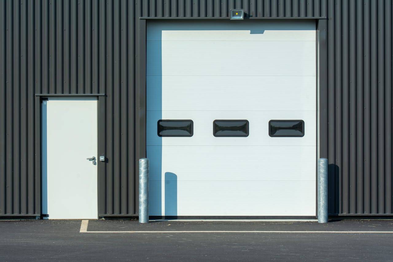 contact-img A modern industrial warehouse facade with a large white garage door and side entrance.