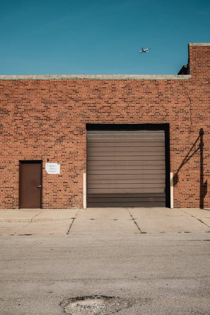 gallery-5 A brick industrial building with a garage door and airplane in the clear sky above.