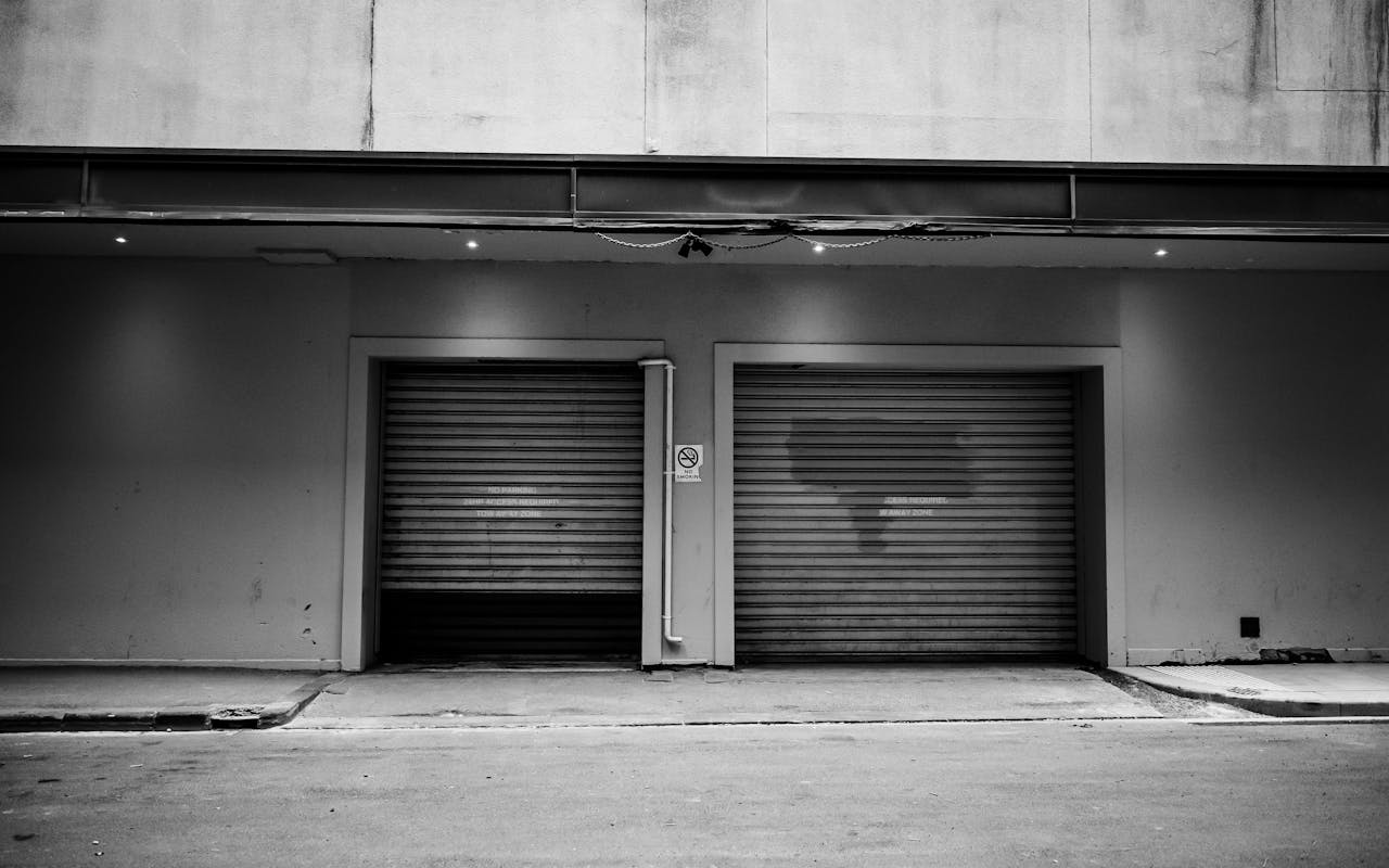 services-02 A monochrome urban exterior with two closed garage doors and a concrete wall.