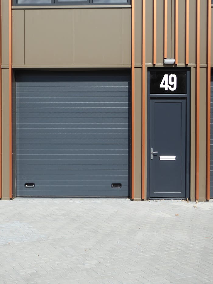 Services-01 A contemporary building facade featuring a dark garage door and entrance with number 49.