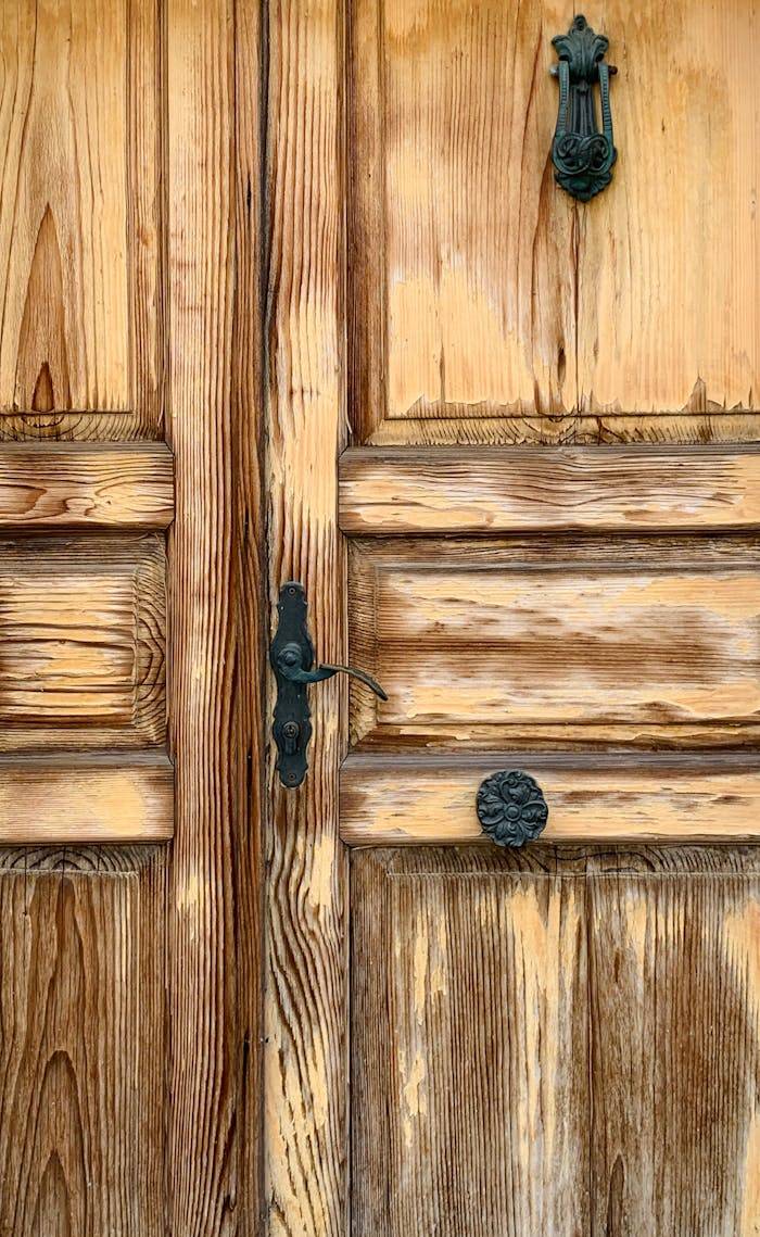 journey Close-up of a rustic wooden door with a vintage metal knocker, showcasing aged texture and craftsmanship.