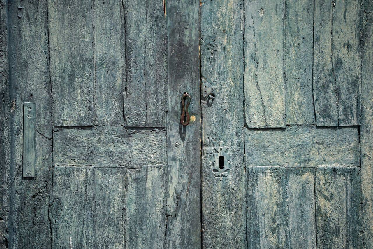 services-01 A vintage turquoise wooden door with rustic textures and an antique lock, showcasing colonial architectural style.