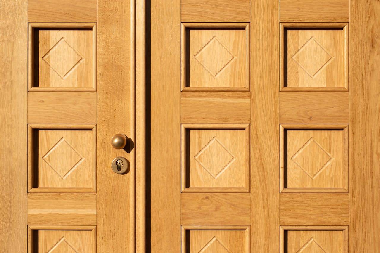 services-03 Close-up of a wooden door featuring geometric diamond patterns and a brass handle.