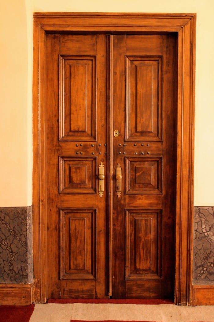 who-we-are Elegant brown wooden double door with brass handles, showcasing classic architectural design.