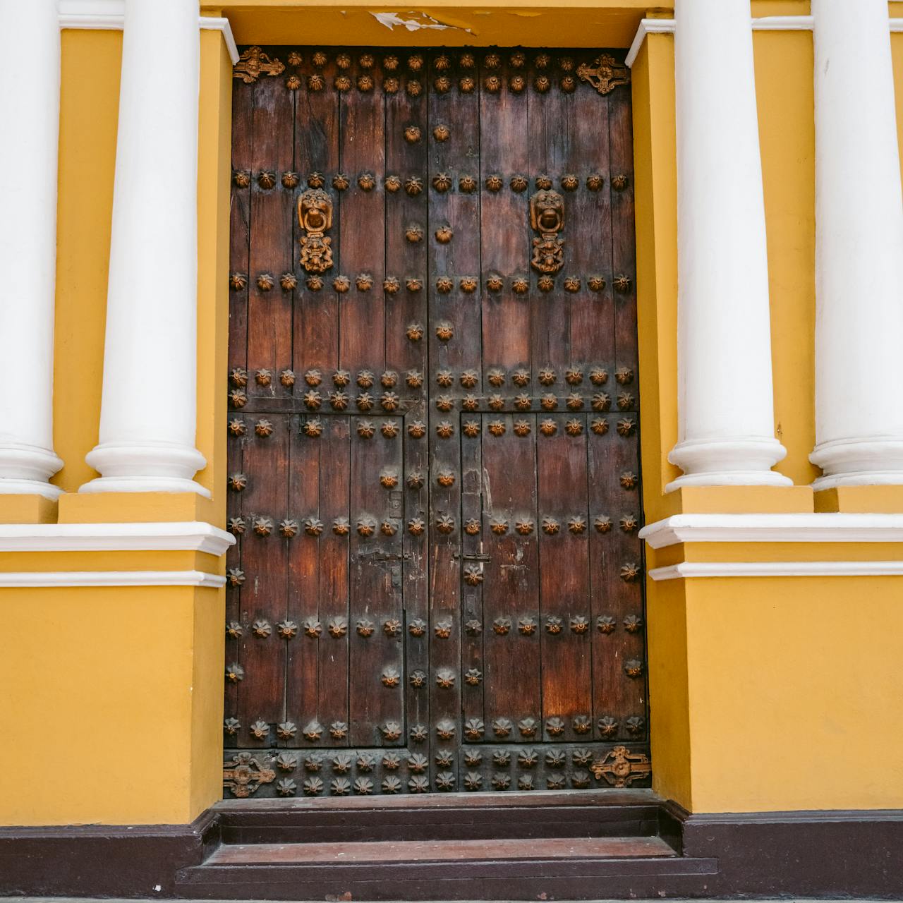team-02 An intricately designed wooden door framed by vibrant yellow columns in Trujillo, Peru.